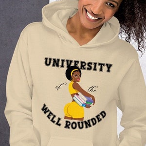 May include: A beige hoodie with a black graphic of a woman holding books. The graphic says "University of the Well Rounded".