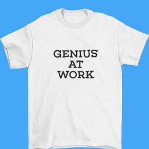 Puede incluir: Camiseta blanca con texto negro que dice "GENIUS AT WORK".