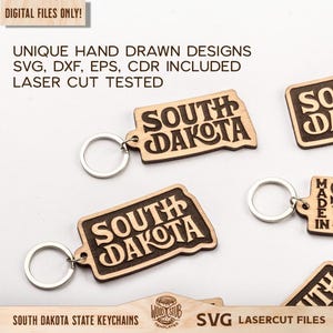 May include: Wooden keychains in the shape of South Dakota with the state name engraved. The keychains have a light brown color with dark brown engraved text. The image also includes the text "DIGITAL FILES ONLY!" and "SVG LASERCUT FILES".