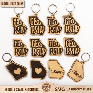 Puede incluir: Un conjunto de 10 llaveros de madera cortados con láser que representan el estado de Georgia. Los llaveros tienen la forma del estado y presentan diferentes diseños, incluyendo las palabras "Made in Georgia", "Geo Relay" y "Home".