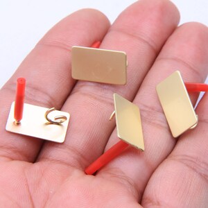 Puede incluir: Cuatro placas de metal de color dorado con asas de plástico rojo. Las placas son rectangulares y tienen esquinas redondeadas. Las asas están unidas a la parte superior de las placas.