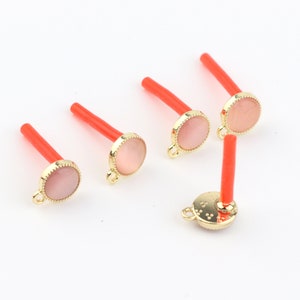 May include: Five gold-toned pendant charms with a pink cabochon stone and a red plastic stick attached to the top.