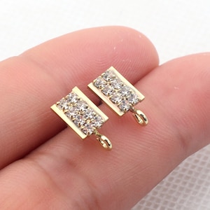May include: Two gold-toned earring charms with a rectangular shape and a clear crystal design. Each charm has a small loop at the bottom.