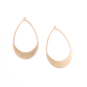 May include: Two gold-colored metal earring blanks in the shape of a teardrop with a rounded bottom. The blanks have a small loop at the top for attaching earring wires.