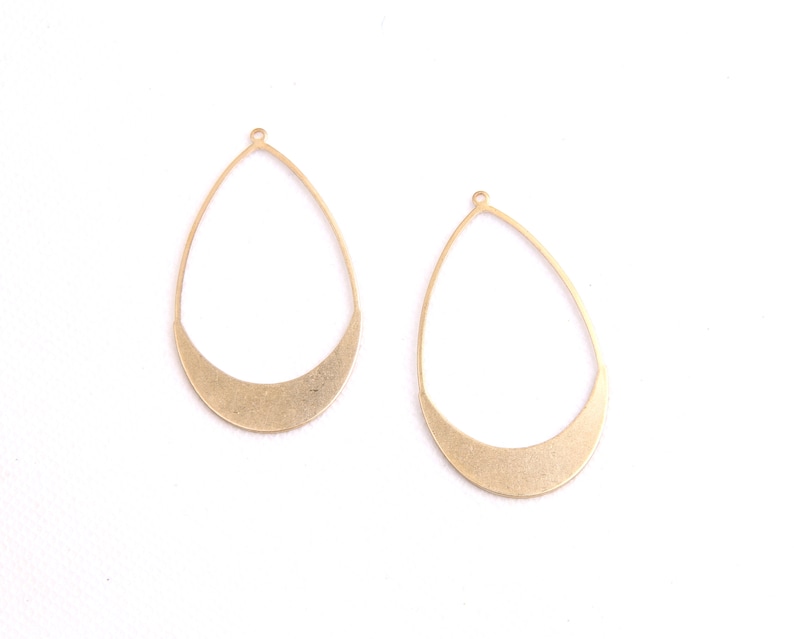 May include: Two gold-colored metal earring blanks in the shape of a teardrop with a rounded bottom. The blanks have a small loop at the top for attaching earring wires.