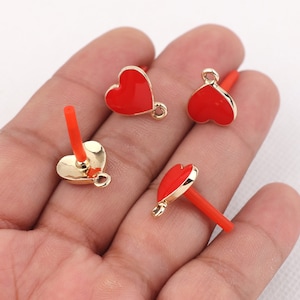 May include: Four gold-colored heart-shaped charms with red enamel. Each charm has a loop for attaching to a necklace, bracelet, or other jewelry.