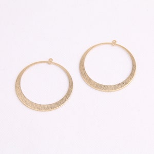 May include: Two gold-toned hoop earrings with a brushed finish. The hoops are circular and have a small loop at the top for attaching to an earring post.
