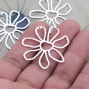 May include: Three silver metal daisy-shaped charms with a hole at the top for attaching to jewelry or other crafts.