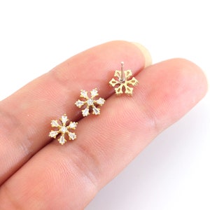 May include: A pair of gold snowflake stud earrings with clear cubic zirconia stones.