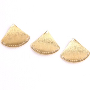 May include: Three gold-colored metal fan-shaped charms with a beaded edge. The charms have a brushed finish and a hole at the top for attaching to jewelry.