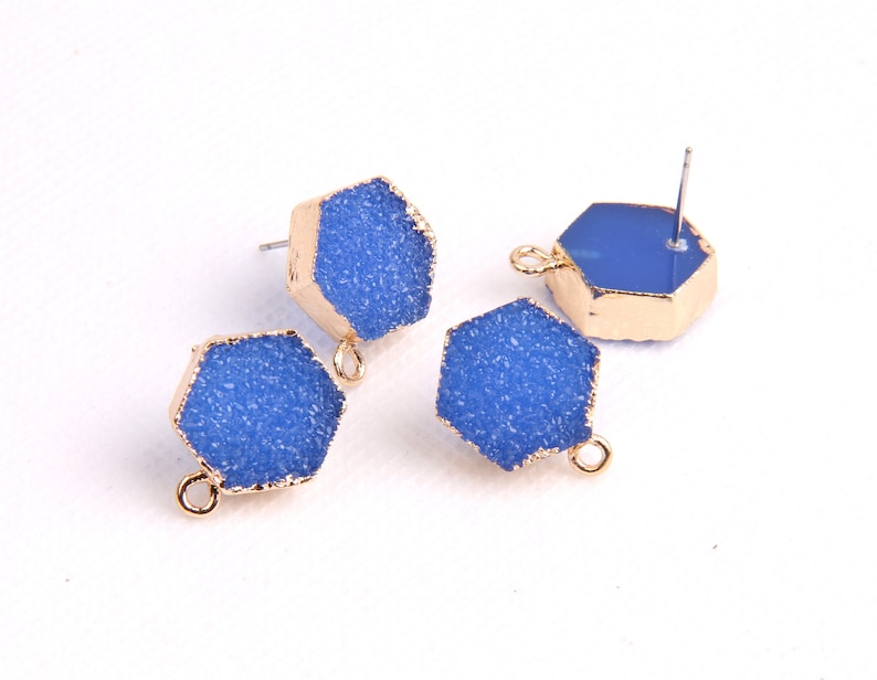 May include: Four blue hexagonal shaped earring charms with gold accents. Two charms have a loop for attaching to a chain or bracelet, and two charms have a post for attaching to an earring.