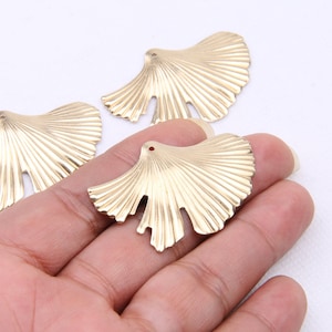 Op de afbeelding: Drie goudkleurige metalen waaiervormige versieringen met een textuur. De versieringen zijn ongeveer 5 cm lang.