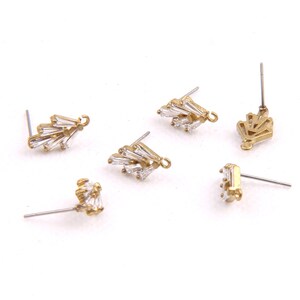 May include: Five gold-tone earring findings with clear crystal accents. The findings are in various shapes, including a fan, a crown, and a cluster of crystals.