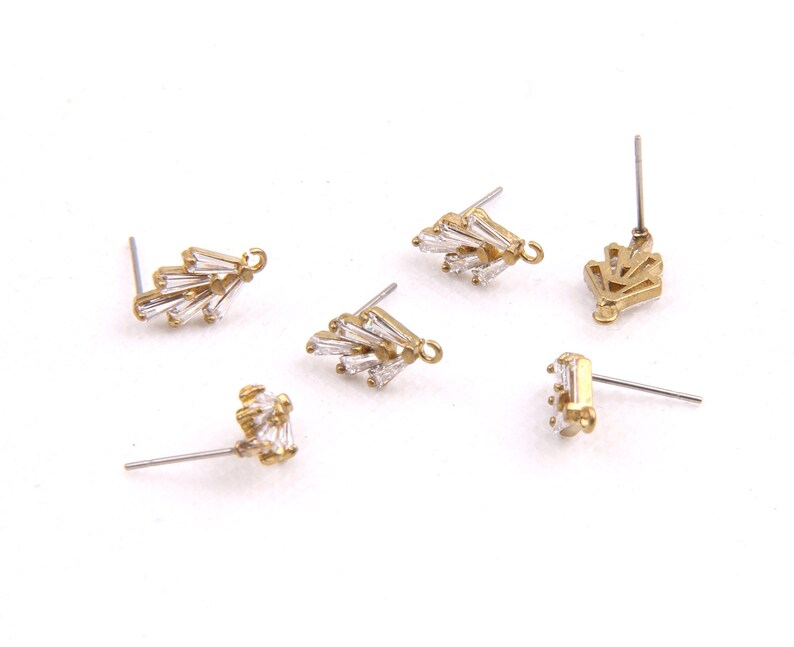 May include: Five gold-tone earring findings with clear crystal accents. The findings are in various shapes, including a fan, a crown, and a cluster of crystals.