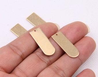 May include: Four gold-colored metal rectangular tags with a hole at the top. The tags are on a hand.
