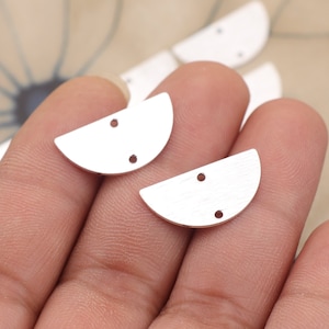 May include: Two silver half-circle metal charms with two holes each. The charms are held in a hand.