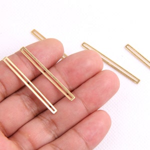 Könnte beinhalten: Vier goldfarbene Metallstangenformen mit einem doppelten Linienmuster. Die Stangen sind in einer Linie auf einer weißen Oberfläche angeordnet.