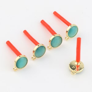 May include: Five gold-toned pendant charms with turquoise-colored cabochons. Each charm has a red plastic stick attached to the top.