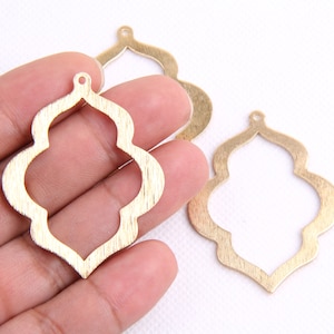 May include: Three gold metal pendant charms with a quatrefoil design. The charms have a brushed finish and a hole at the top for hanging.