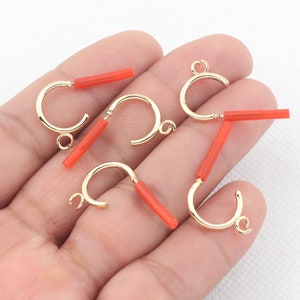 May include: Six gold hoop earring findings with red plastic tubes attached to the hoops. The hoops are open and the tubes are inserted through the hoops.