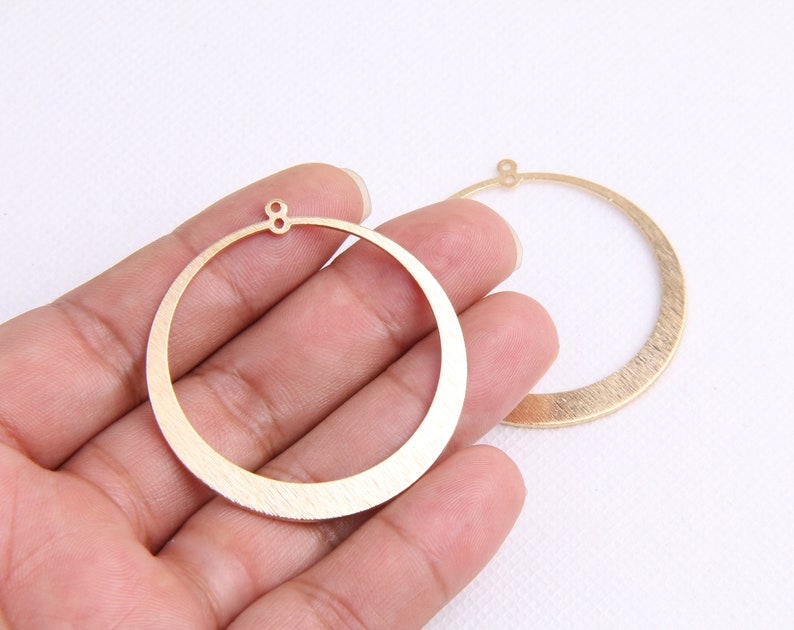 May include: Two gold-toned metal hoops with a brushed finish. The hoops are circular and have a small hole at the top for attaching to earrings.