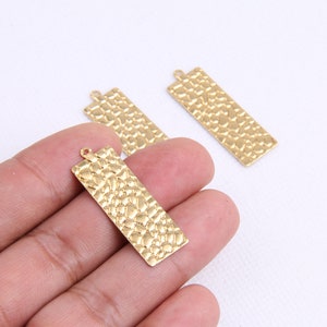 May include: Three gold-colored metal rectangular pendant charms with a textured surface. The charms have a hole at the top for attaching to a necklace or bracelet.