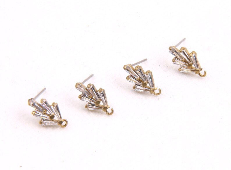 May include: Three gold-tone earring findings with clear crystal accents. Each finding has a small loop at the bottom.