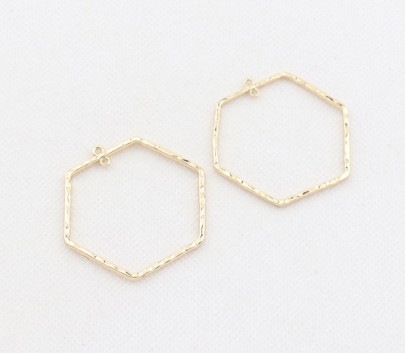 Op de afbeelding: Twee gouden zeshoekige hoepels met een textuur. De hoepels hebben een springring sluiting.