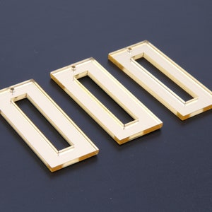 May include: Three gold acrylic rectangular shapes with a smaller rectangle cut out in the center of each.
