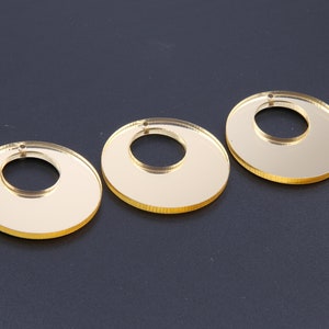 May include: Three gold-coloured, round, acrylic, mirror-like ornaments with a hole in the centre.