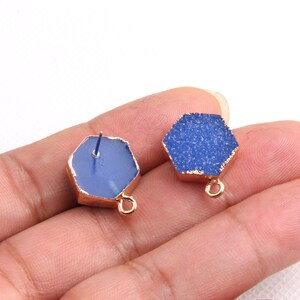 May include: Two blue hexagon-shaped gemstone pendants with gold-toned edges and a loop for hanging. The pendants have a textured, sparkly surface.
