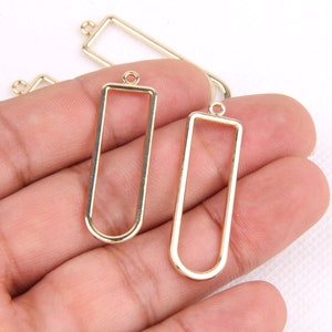 May include: Three gold metal rectangular frames with a loop at the top for hanging. The frames are different sizes and are perfect for adding a personal touch to jewelry.