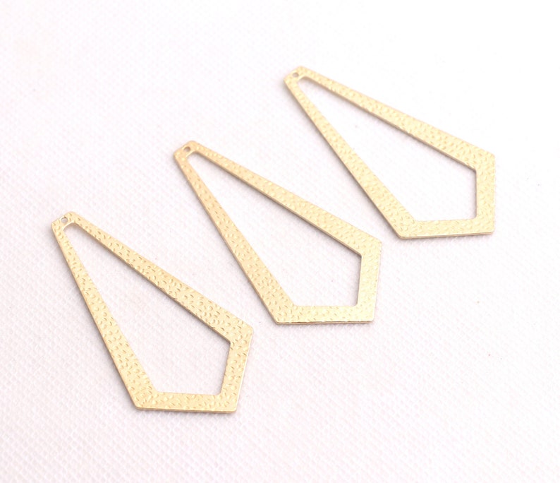 May include: Three gold-colored metal geometric shapes with a textured surface. The shapes are open and resemble a long, narrow diamond.