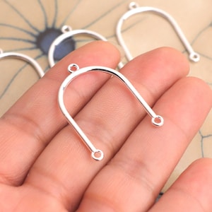 May include: Close-up of several silver-colored, U-shaped jewelry components. Each component has a rounded top and two straight, parallel sides with small holes at the ends. The components are likely for earrings or pendants.