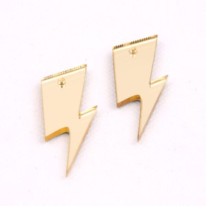 May include: Two gold lightning bolt shaped earrings. The earrings are made of acrylic and have a mirrored finish.