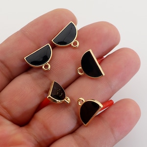 Op de afbeelding: Vijf goudkleurige metalen halve cirkelcharms met zwart email. Elke charme heeft een springring.