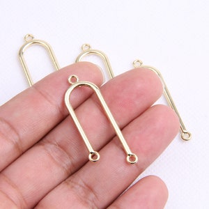 May include: Four gold-toned metal arch-shaped jewelry findings with two loops at the top and one loop at the bottom.