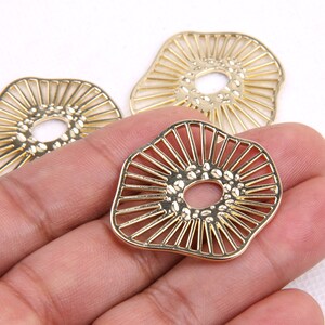 May include: Three gold metal decorative charms with a sunburst design and a textured center hole. The charms are in the shape of a circle with a wavy edge.