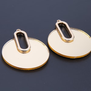 May include: A pair of gold-toned earrings with a circular design. Each earring features a large, round, mirrored disc with a smaller oval cutout in the centre.