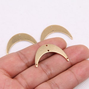 May include: Three gold-toned metal crescent moon shapes with two holes each. The crescent moons are approximately 2 inches in length.