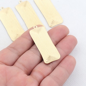 May include: Four gold-colored metal rectangular tags with a decorative, concentric circle pattern. The tags have a hole at the top for hanging.