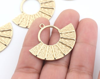 May include: Gold metal pendant with a fan-shaped design and a circular opening in the center. The pendant has a textured surface and is perfect for jewelry making.