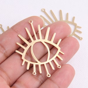 May include: Gold metal eye charm with a detailed design and a fringe of rays. The charm has two holes for attaching to jewellery or other crafts.