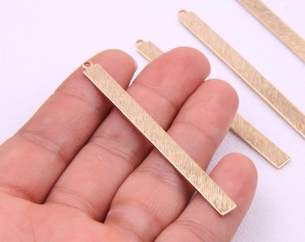 May include: Four gold-colored metal bar pendants with a brushed finish. Each pendant has a small loop at the top for attaching to a chain or cord.