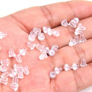 May include: A close-up of a hand holding a large quantity of clear plastic earring backs.
