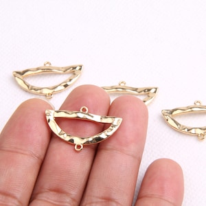 Pode incluir: Quatro formas de semicírculo de metal dourado com textura martelada e dois anéis de salto em cada um. Os semicírculos estão dispostos em uma fila sobre uma superfície branca.