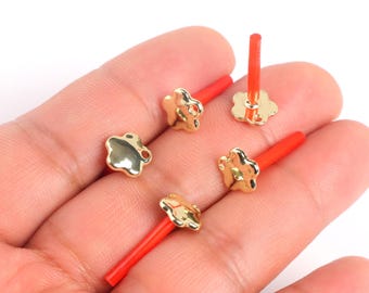 May include: Five gold-colored flower-shaped charms with a hole in the center. The charms are attached to red plastic sticks.