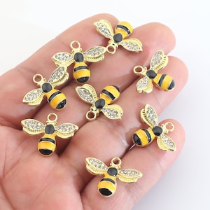 May include: Eight gold bee charms with black and yellow enamel and clear rhinestones. The bee charms have a loop at the top for attaching to jewelry.