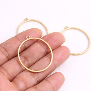 Pode incluir: Três argolas de metal douradas com um anel de salto na parte superior. As argolas são de tamanhos diferentes e estão dispostas em fila.