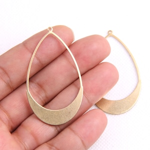 May include: Two gold-toned metal teardrop-shaped earring blanks with a rounded bottom edge. The blanks have a small loop at the top for attaching earring wires.